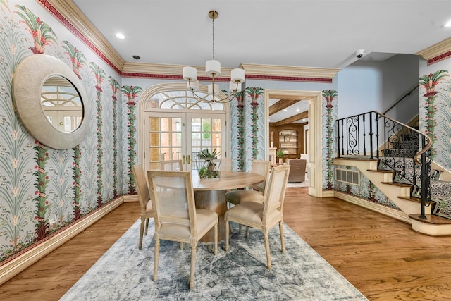 dining space featuring wood-type flooring, french doors, a wall mounted air conditioner, crown molding, and a chandelier