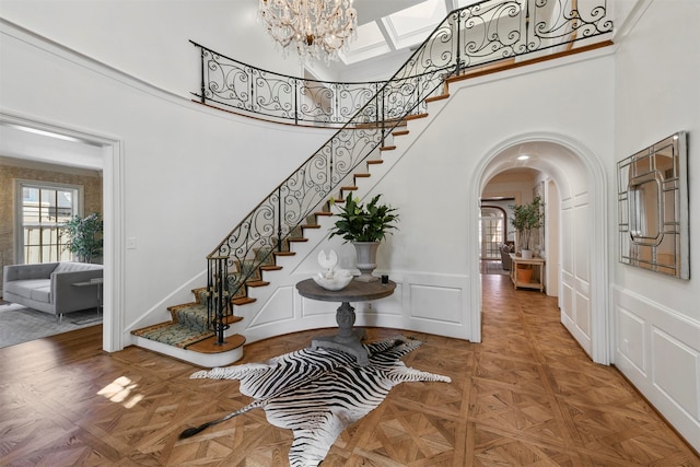 entrance foyer featuring parquet floors, a towering ceiling, and an inviting chandelier