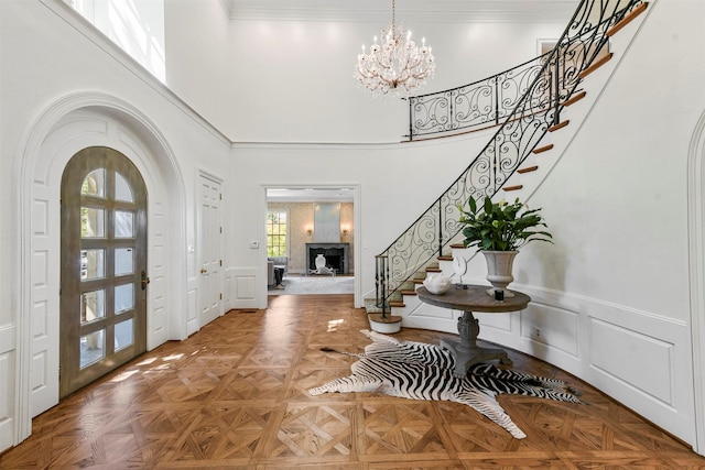 foyer with a towering ceiling, ornamental molding, an inviting chandelier, and parquet floors