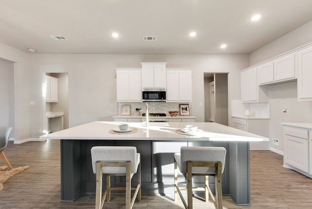 kitchen featuring a kitchen bar, stove, a kitchen island with sink, dark hardwood / wood-style floors, and white cabinetry