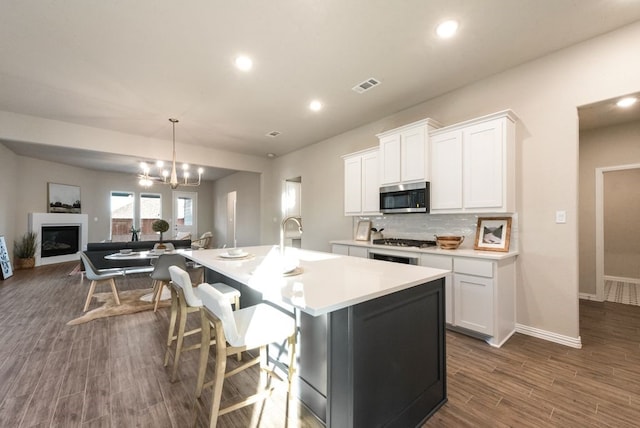 kitchen with sink, an island with sink, tasteful backsplash, decorative light fixtures, and white cabinetry