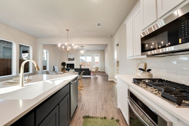 kitchen with light wood-type flooring, white cabinetry, stainless steel appliances, and hanging light fixtures