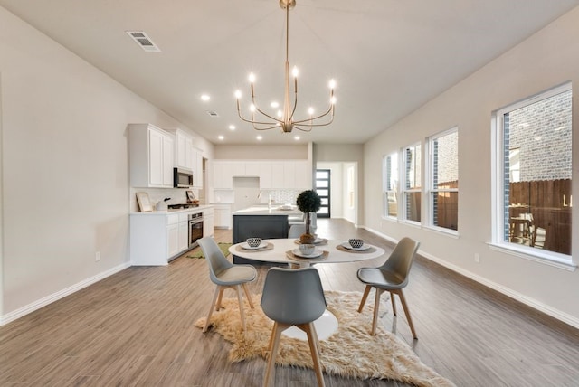 dining space with light wood-type flooring, sink, and an inviting chandelier