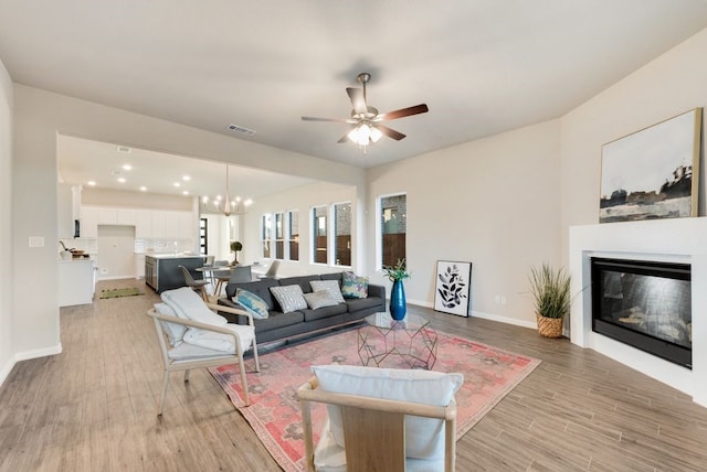 living room featuring ceiling fan with notable chandelier and light hardwood / wood-style flooring