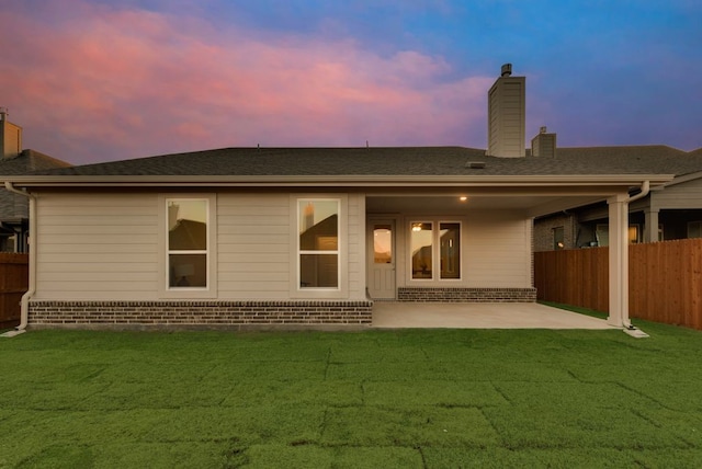 back house at dusk featuring a yard and a patio