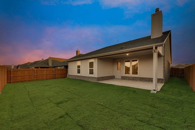 back house at dusk with a yard and a patio