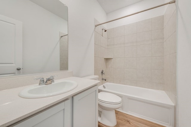 full bathroom with hardwood / wood-style flooring, tiled shower / bath combo, vanity, and toilet