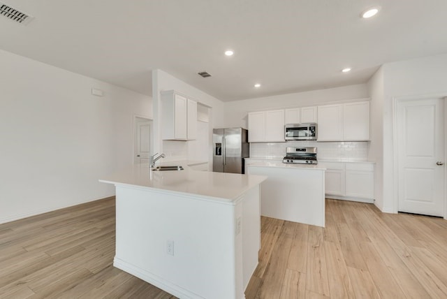 kitchen featuring appliances with stainless steel finishes, backsplash, light hardwood / wood-style floors, and an island with sink