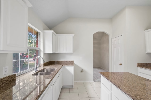 kitchen featuring dark stone counters, white cabinets, sink, lofted ceiling, and light tile patterned flooring