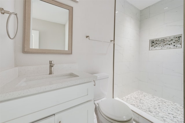 bathroom with a tile shower, vanity, and toilet