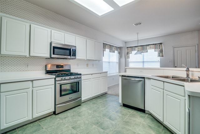 kitchen featuring appliances with stainless steel finishes, white cabinetry, pendant lighting, and sink