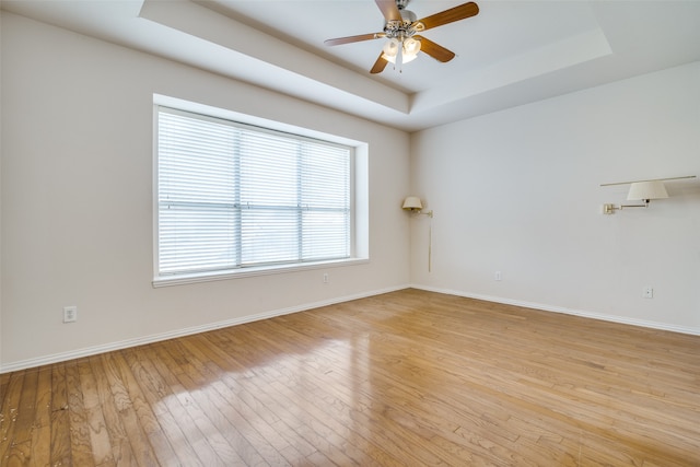 empty room featuring a raised ceiling, ceiling fan, and light hardwood / wood-style flooring