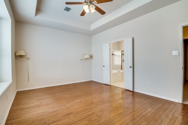 empty room with ceiling fan, light wood-type flooring, and a tray ceiling