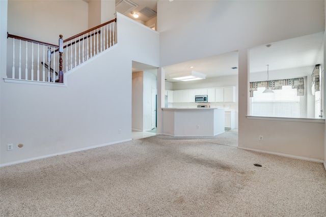 unfurnished living room featuring light carpet and a high ceiling