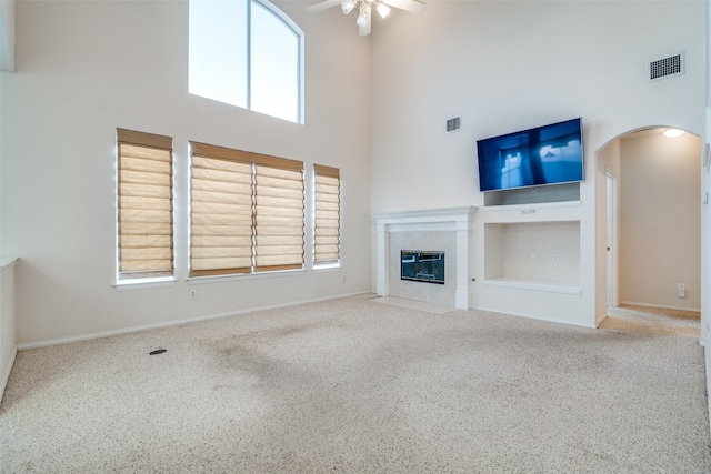 unfurnished living room featuring carpet flooring, ceiling fan, a healthy amount of sunlight, and a tiled fireplace