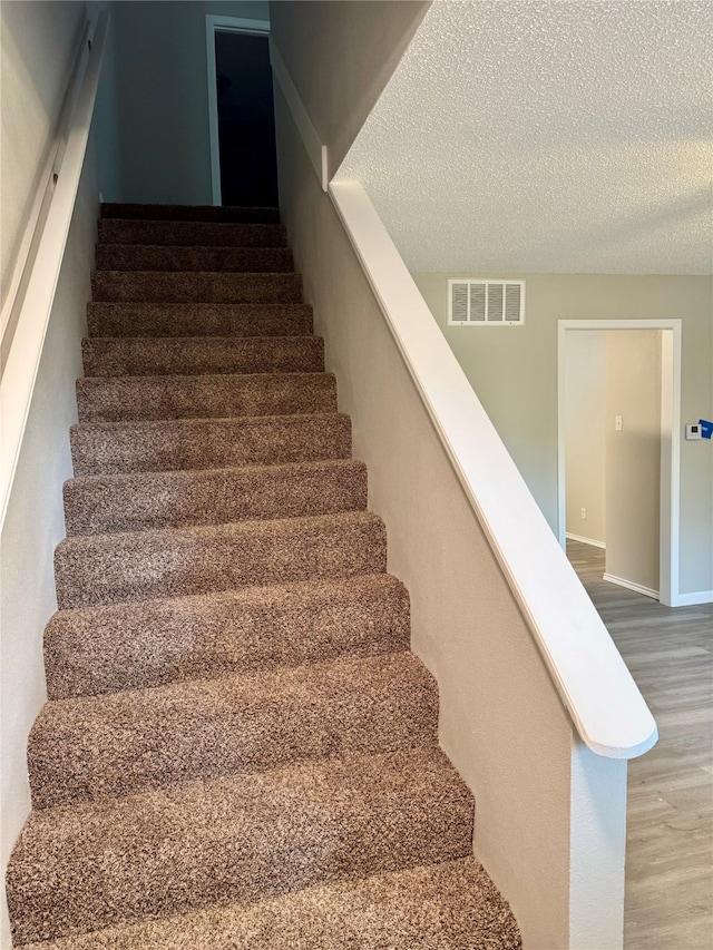 stairs with a textured ceiling and hardwood / wood-style flooring