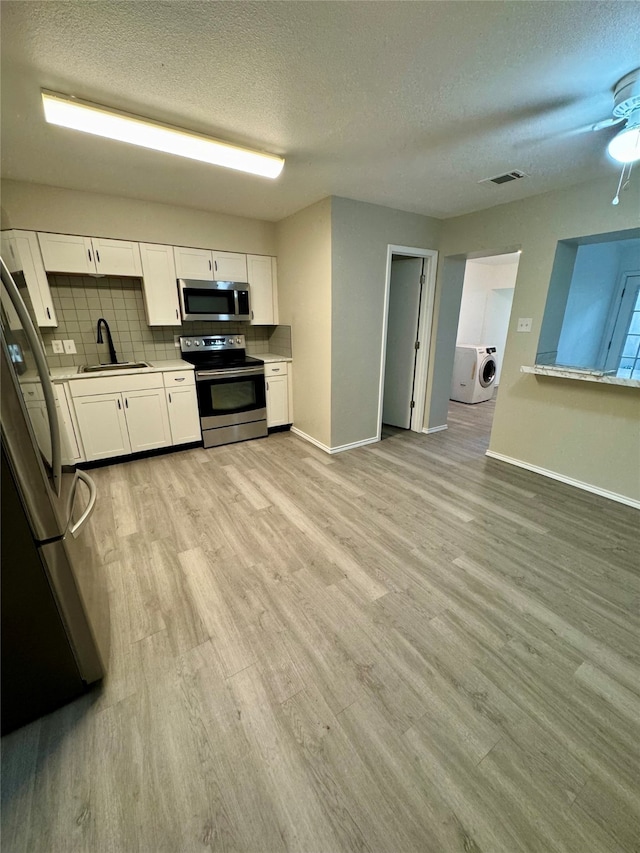 kitchen featuring light hardwood / wood-style floors, washer / dryer, stainless steel appliances, sink, and white cabinetry