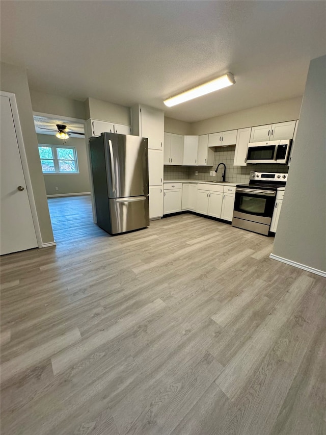 kitchen featuring light hardwood / wood-style flooring, appliances with stainless steel finishes, white cabinetry, sink, and ceiling fan