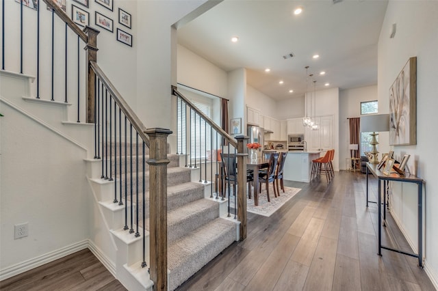 stairs with hardwood / wood-style flooring, a high ceiling, and an inviting chandelier