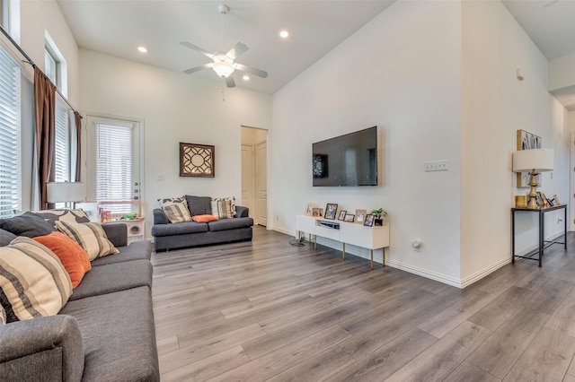 living room featuring a high ceiling, plenty of natural light, ceiling fan, and light wood-type flooring