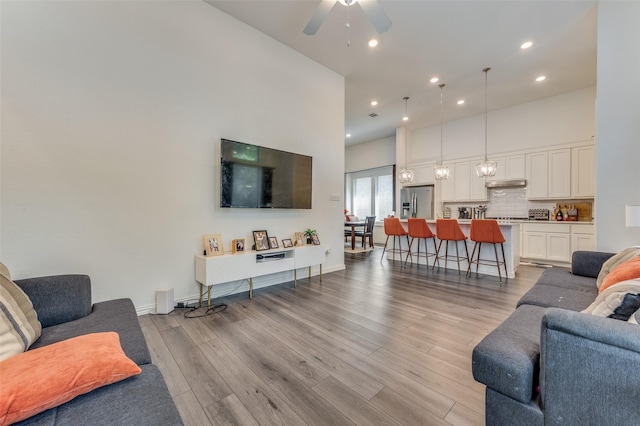 living room with ceiling fan, light wood-type flooring, and a high ceiling