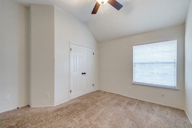 spare room featuring light carpet, vaulted ceiling, a textured ceiling, and ceiling fan