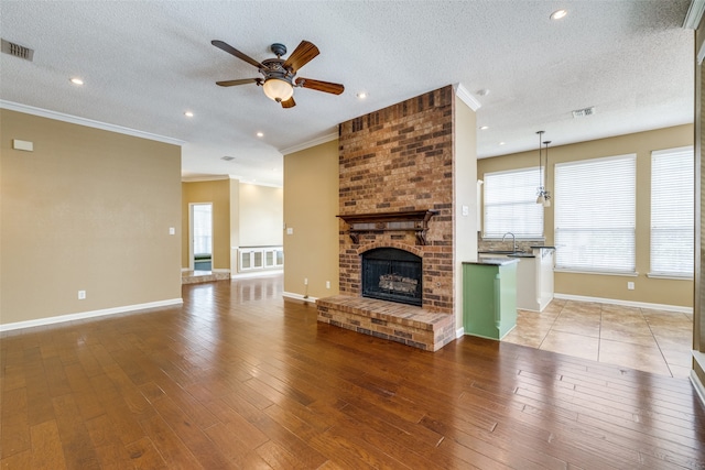 unfurnished living room featuring a textured ceiling, a fireplace, wood-type flooring, sink, and ceiling fan