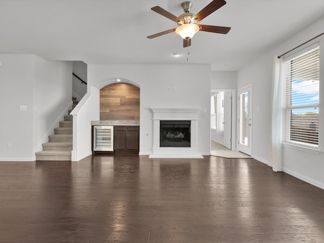 unfurnished living room with beverage cooler, ceiling fan, and dark hardwood / wood-style flooring