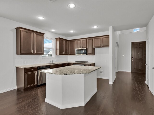 kitchen with light stone counters, dark hardwood / wood-style floors, sink, a kitchen island, and stainless steel appliances