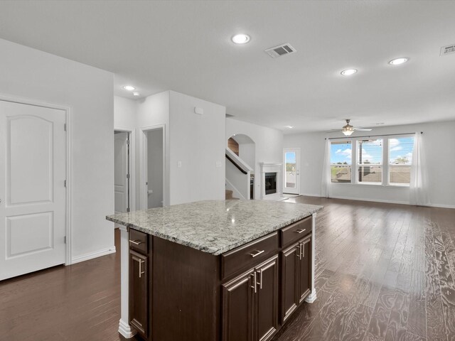 kitchen featuring light stone counters, a kitchen island, ceiling fan, dark brown cabinetry, and dark hardwood / wood-style floors