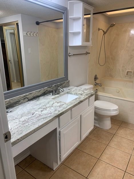 full bathroom with washtub / shower combination, tile patterned flooring, toilet, and vanity