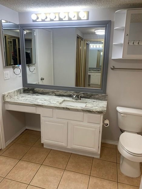 bathroom featuring tile patterned flooring, vanity, toilet, and a textured ceiling