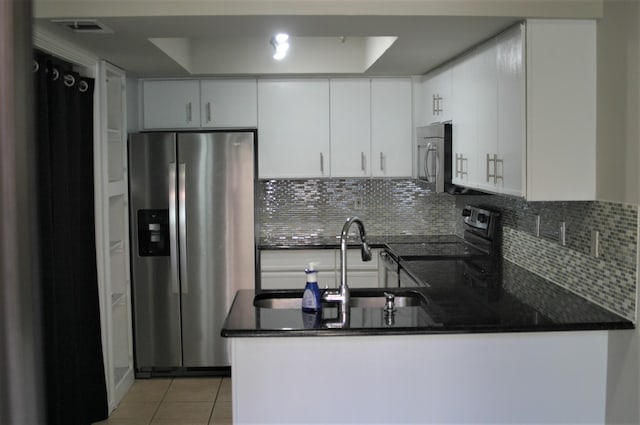 kitchen featuring stainless steel appliances, white cabinetry, a tray ceiling, kitchen peninsula, and decorative backsplash