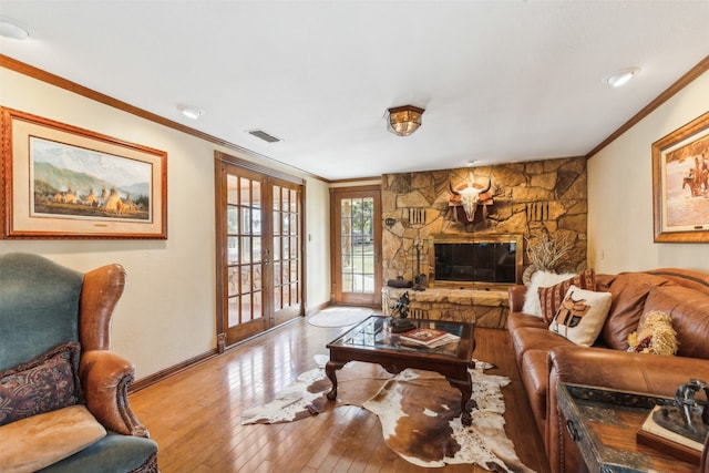 living room with french doors, a stone fireplace, ornamental molding, and light hardwood / wood-style flooring