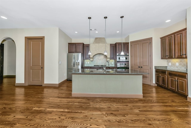 kitchen featuring hanging light fixtures, stainless steel appliances, dark hardwood / wood-style flooring, and a kitchen island with sink