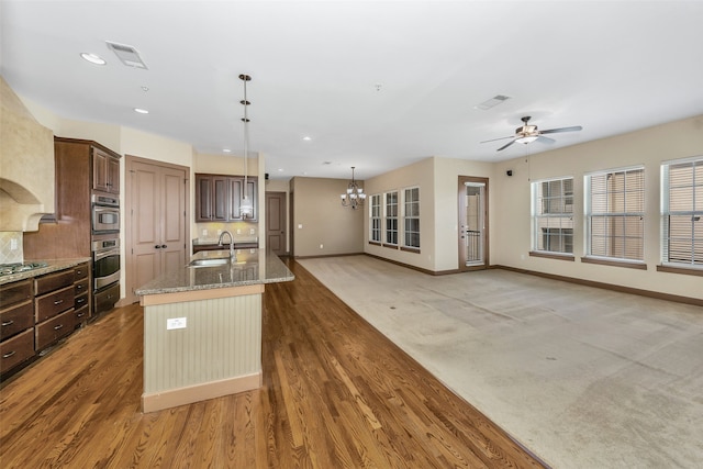 kitchen featuring ceiling fan with notable chandelier, light stone counters, sink, a center island with sink, and dark brown cabinetry