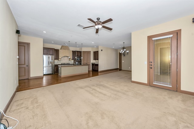 unfurnished living room featuring light colored carpet and ceiling fan with notable chandelier