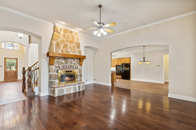 unfurnished living room with ceiling fan with notable chandelier, a stone fireplace, ornamental molding, and dark hardwood / wood-style flooring