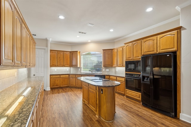 kitchen with black appliances, crown molding, wood-type flooring, a center island, and dark stone counters