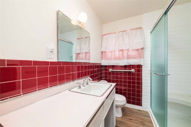 bathroom with vanity, a shower with shower door, wood-type flooring, tile walls, and toilet