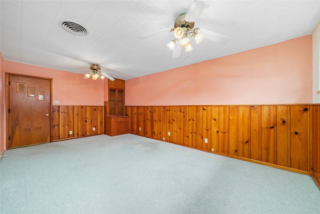 carpeted spare room featuring wood walls and ceiling fan