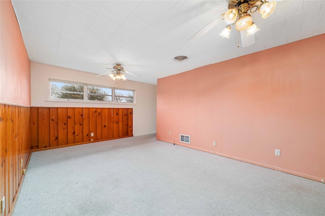 carpeted empty room with ceiling fan and wooden walls