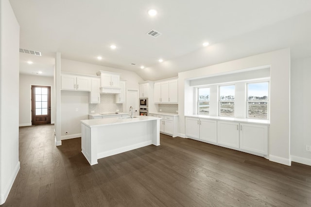 kitchen featuring white cabinetry, sink, vaulted ceiling, a center island with sink, and dark hardwood / wood-style floors