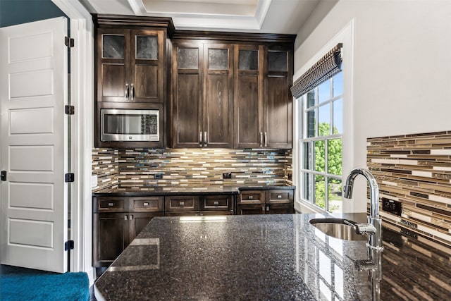 kitchen featuring stainless steel microwave, dark brown cabinets, dark stone countertops, and a healthy amount of sunlight