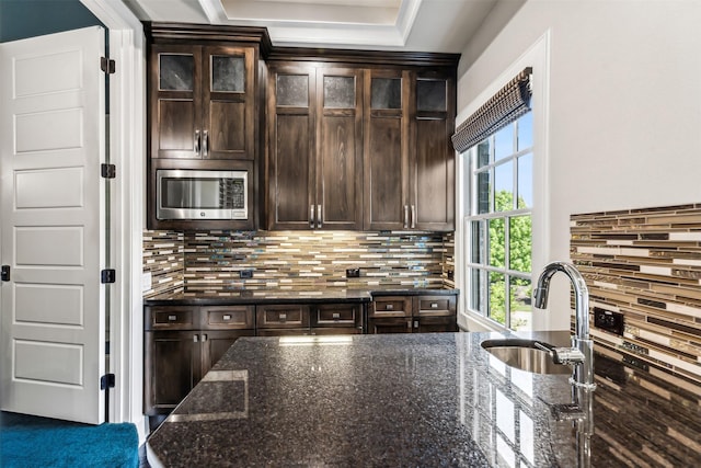 kitchen featuring dark stone counters, dark brown cabinetry, a sink, and stainless steel microwave