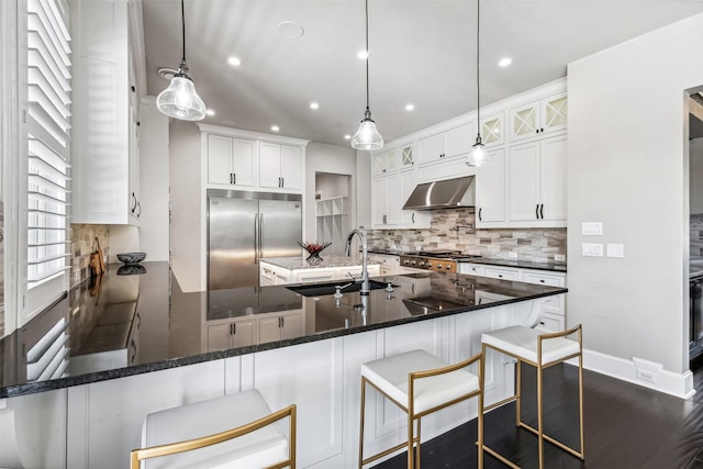 kitchen with tasteful backsplash, recessed lighting, stainless steel built in fridge, a sink, and wall chimney exhaust hood