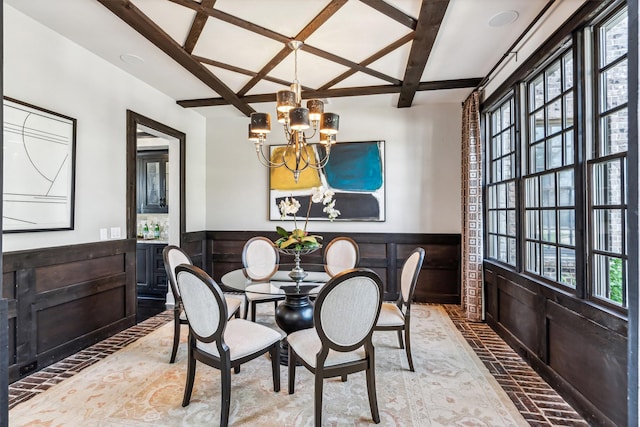 dining area featuring a chandelier, coffered ceiling, beam ceiling, brick floor, and wainscoting