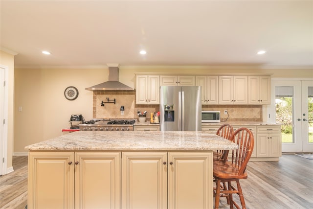 kitchen with light hardwood / wood-style flooring, french doors, light stone counters, wall chimney exhaust hood, and appliances with stainless steel finishes