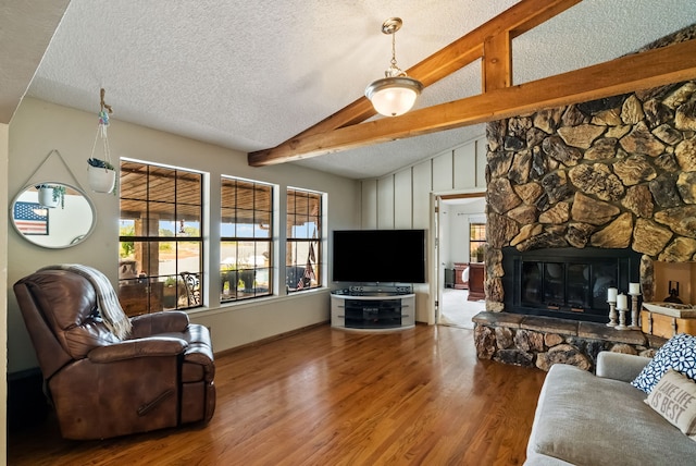 living room with hardwood / wood-style flooring, a textured ceiling, lofted ceiling with beams, and a stone fireplace