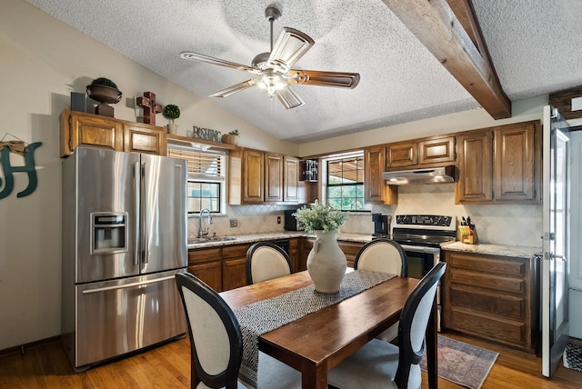 kitchen with a textured ceiling, beamed ceiling, appliances with stainless steel finishes, light hardwood / wood-style floors, and ceiling fan